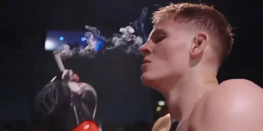 Молодой боец MMA с короткими волосами выдыхает дым от самокрутки в клетке